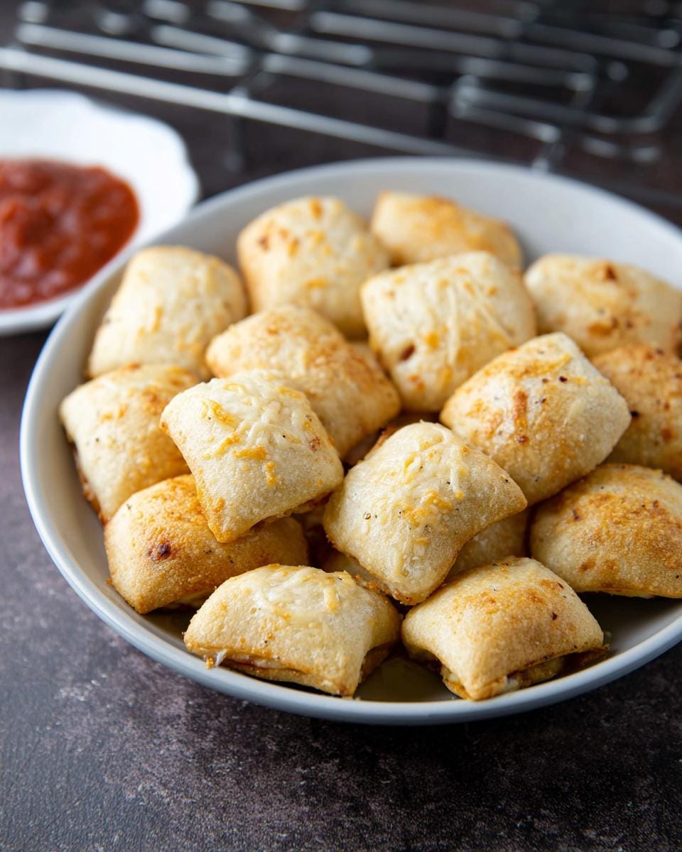 A bowl filled with golden brown, crispy air fryer pizza rolls, served with a side of marinara sauce.