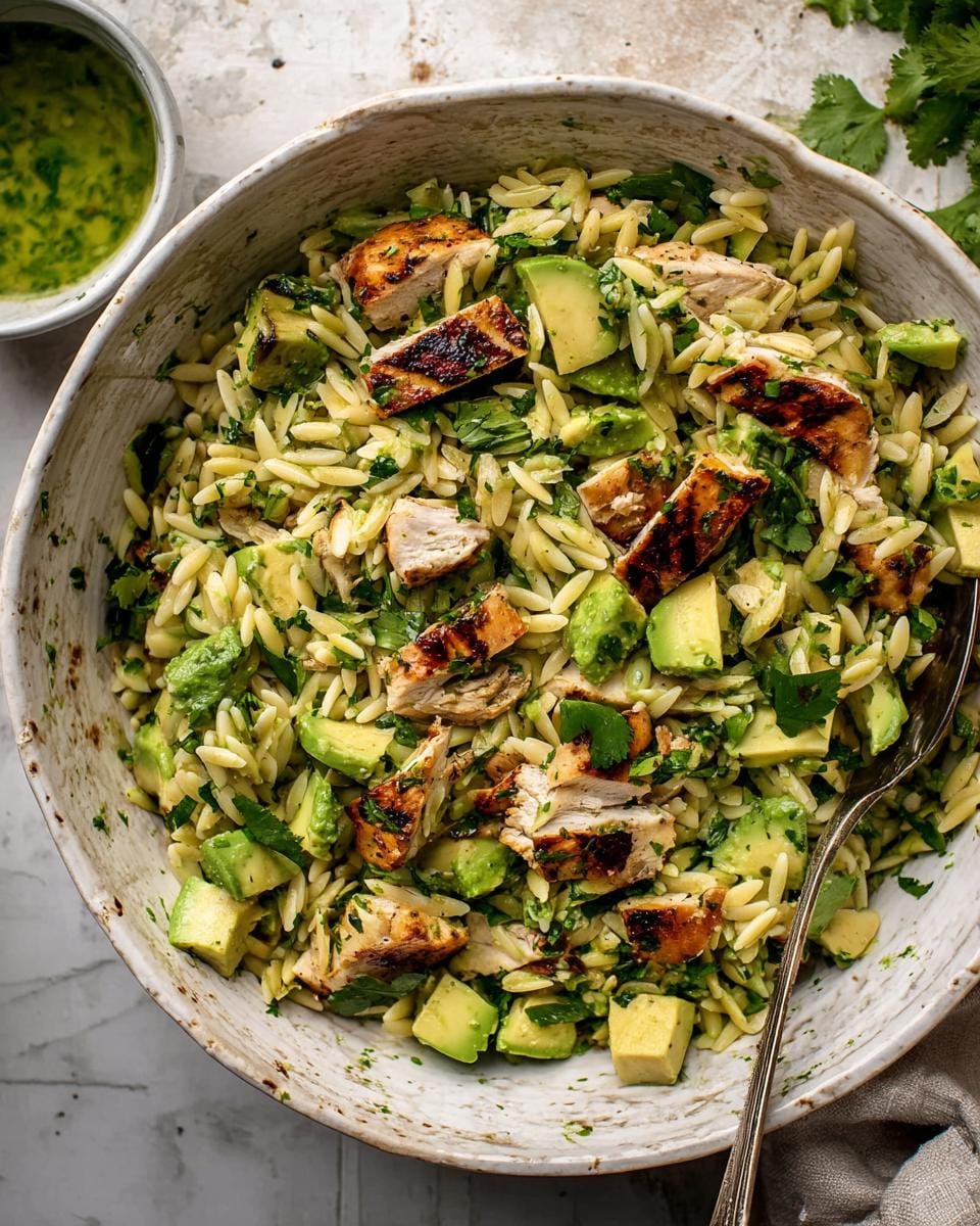 A close-up overhead view of a bowl filled with Grilled Chicken Avocado Orzo Salad, featuring grilled chicken pieces, diced avocado, and orzo pasta.