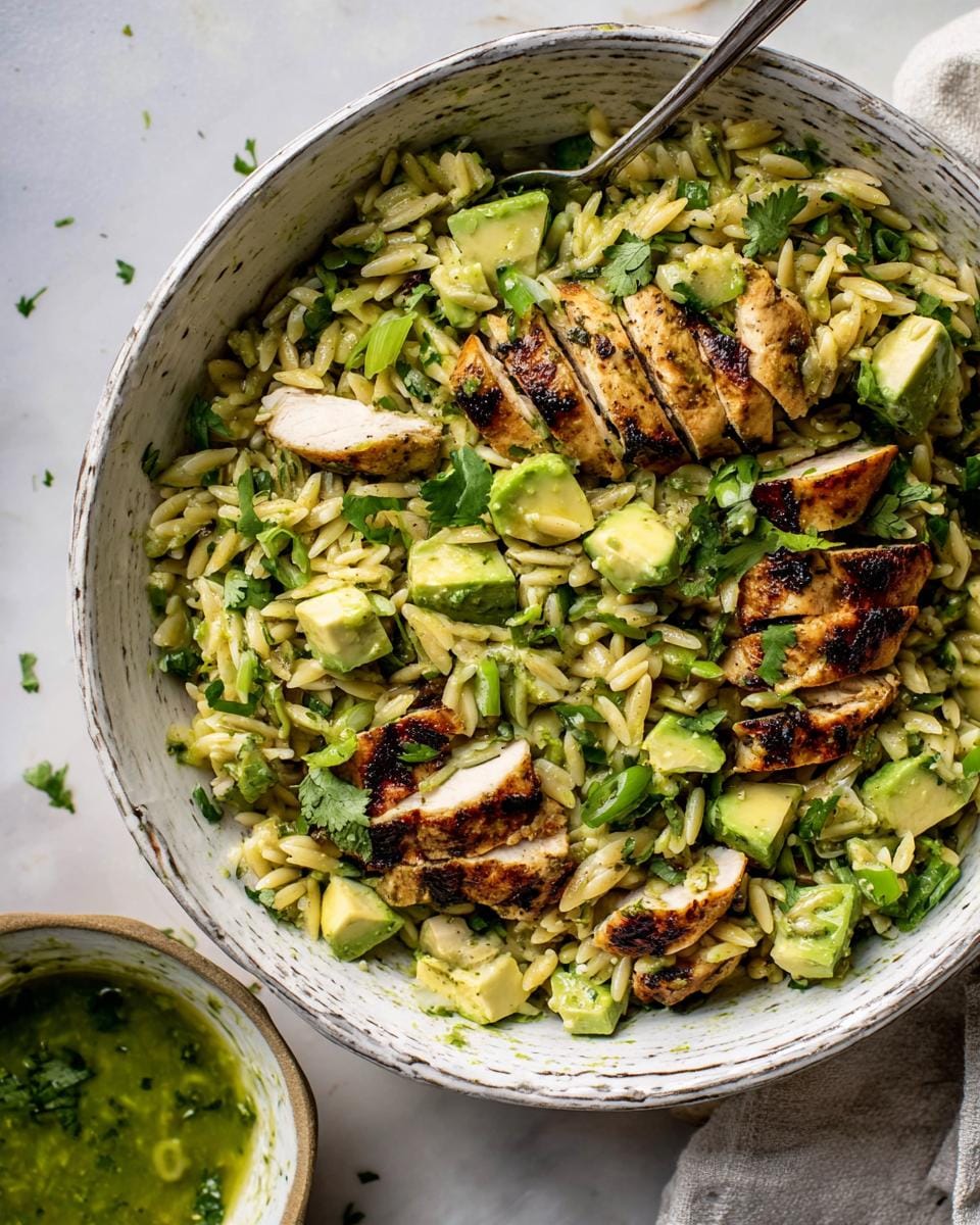 A close-up overhead view of a vibrant Grilled Chicken Avocado Orzo Salad served in a rustic bowl, topped with sliced grilled chicken and fresh avocado.