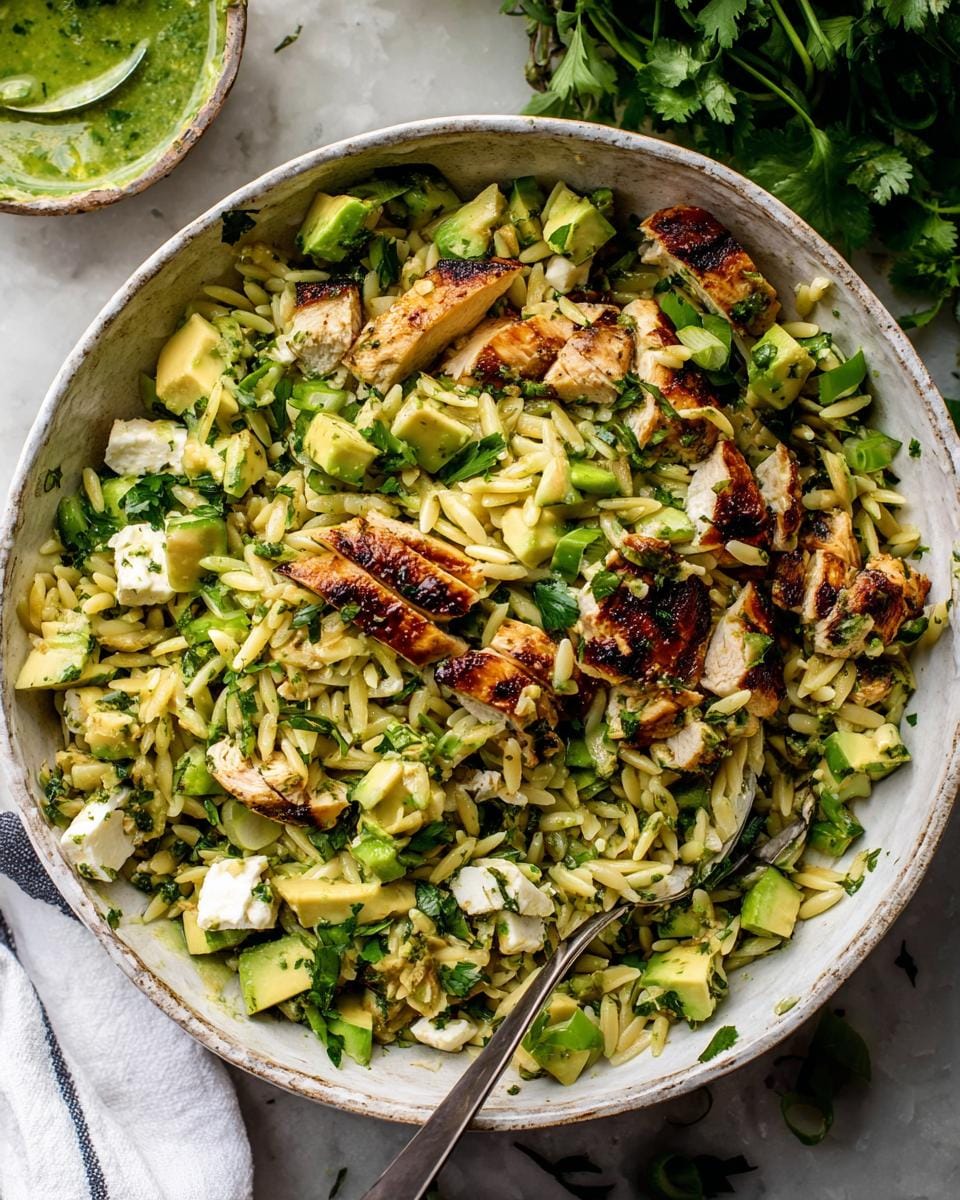 A close-up overhead view of a large bowl filled with Grilled Chicken Avocado Orzo Salad, featuring grilled chicken slices, diced avocado, feta cheese, and fresh herbs.