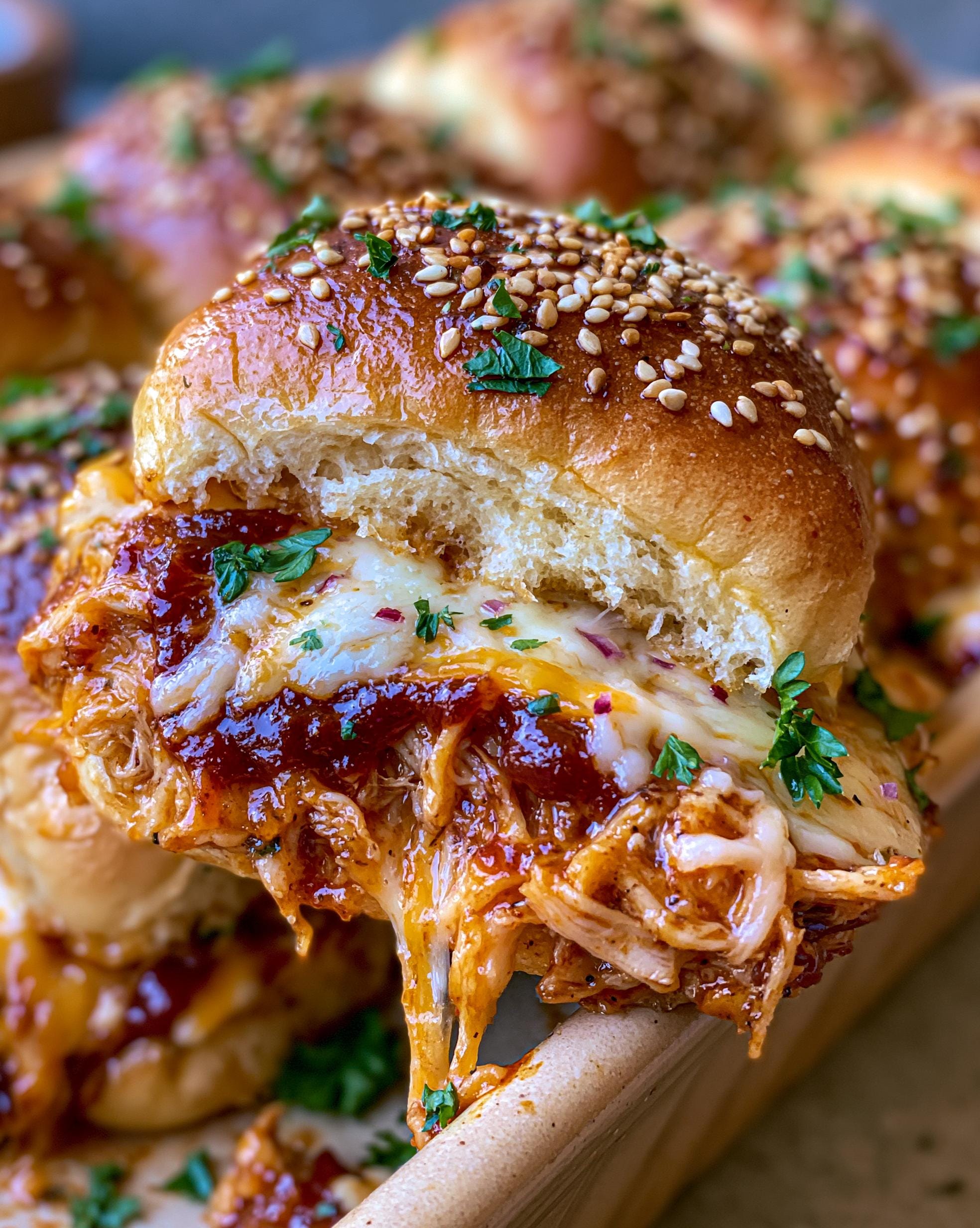 Close-up of a gooey BBQ Chicken Slider with melted cheese and sesame seed bun.