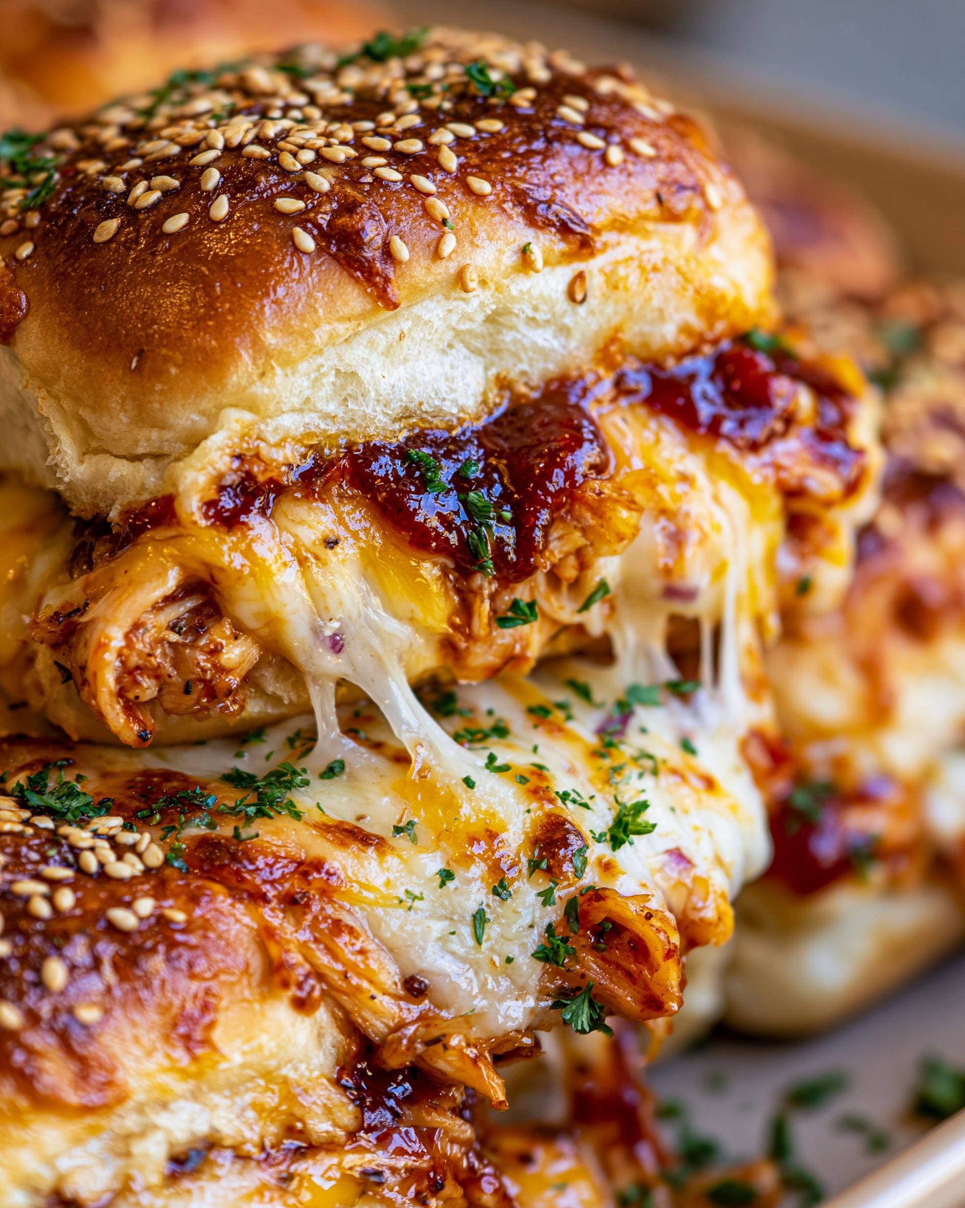 Close-up of stacked BBQ Chicken Sliders with gooey melted cheese and sesame seed buns.