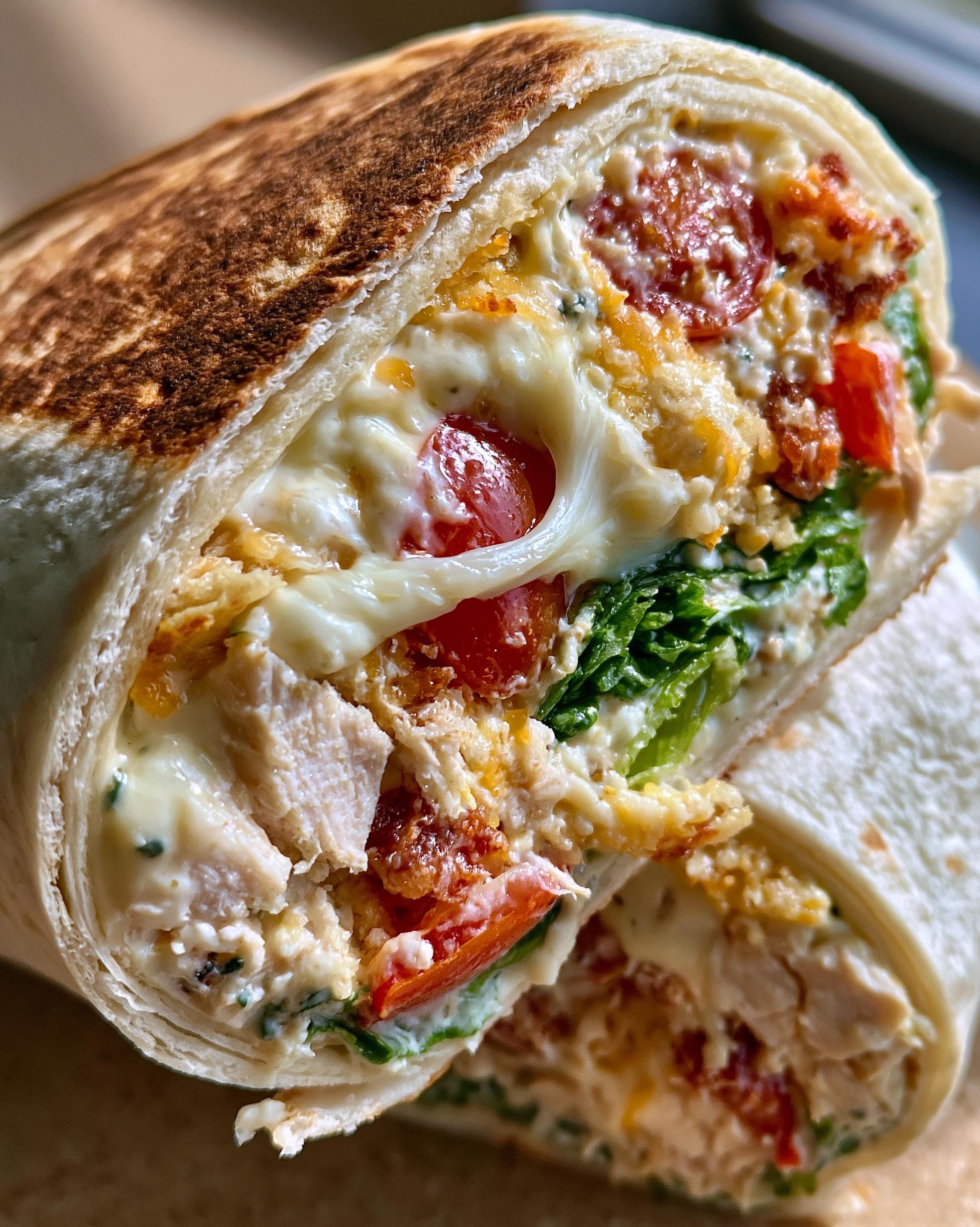 A close-up of a halved Chicken Caesar Wrap, revealing grilled chicken, romaine lettuce, cherry tomatoes, and creamy Caesar dressing.