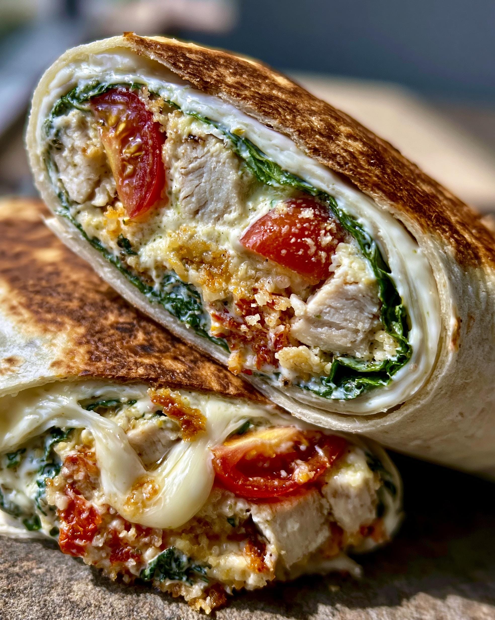 Close-up of a sliced Chicken Caesar Wrap filled with grilled chicken, spinach, tomatoes, and melted cheese.