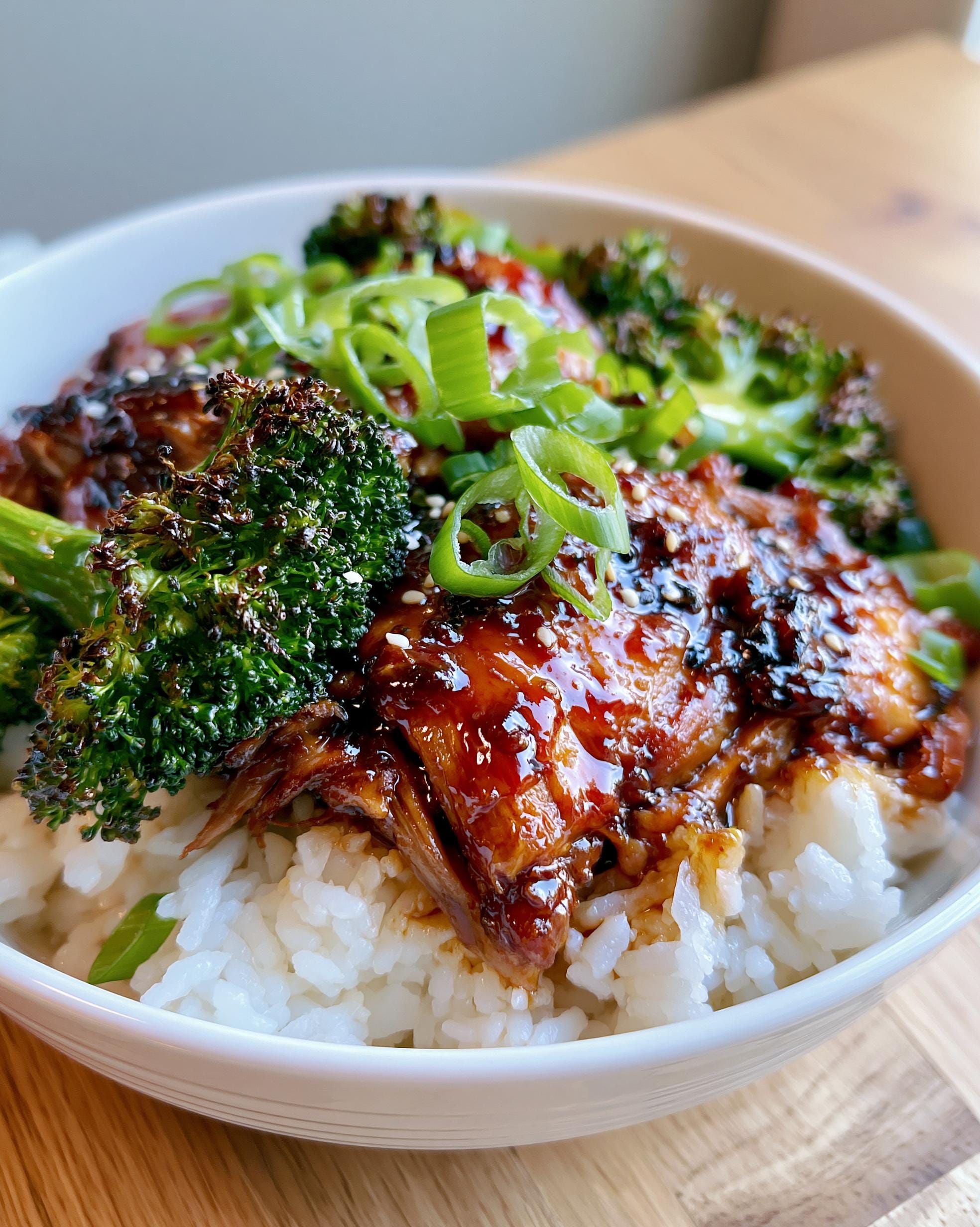 A close-up of a Honey Garlic Chicken meal prep bowl with rice, roasted broccoli, and green onions.