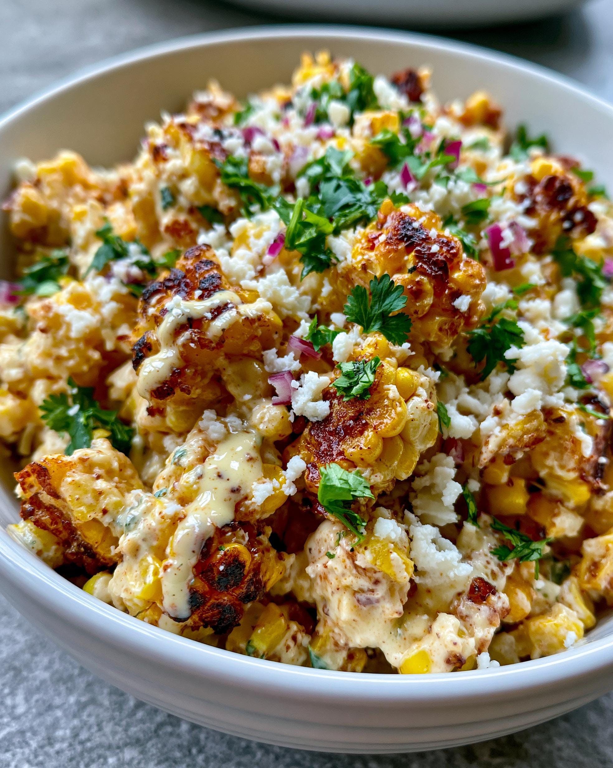 A close-up of Mexican Street Corn Salad in a white bowl, featuring charred corn, creamy dressing, crumbled cotija cheese, and fresh cilantro.