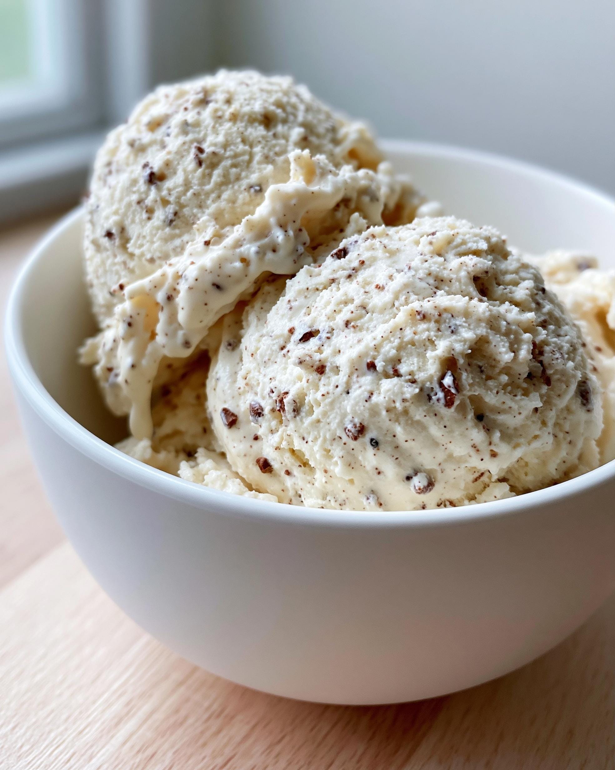 Close-up of scoops of creamy Protein Ice Cream with visible chocolate chunks in a white bowl.