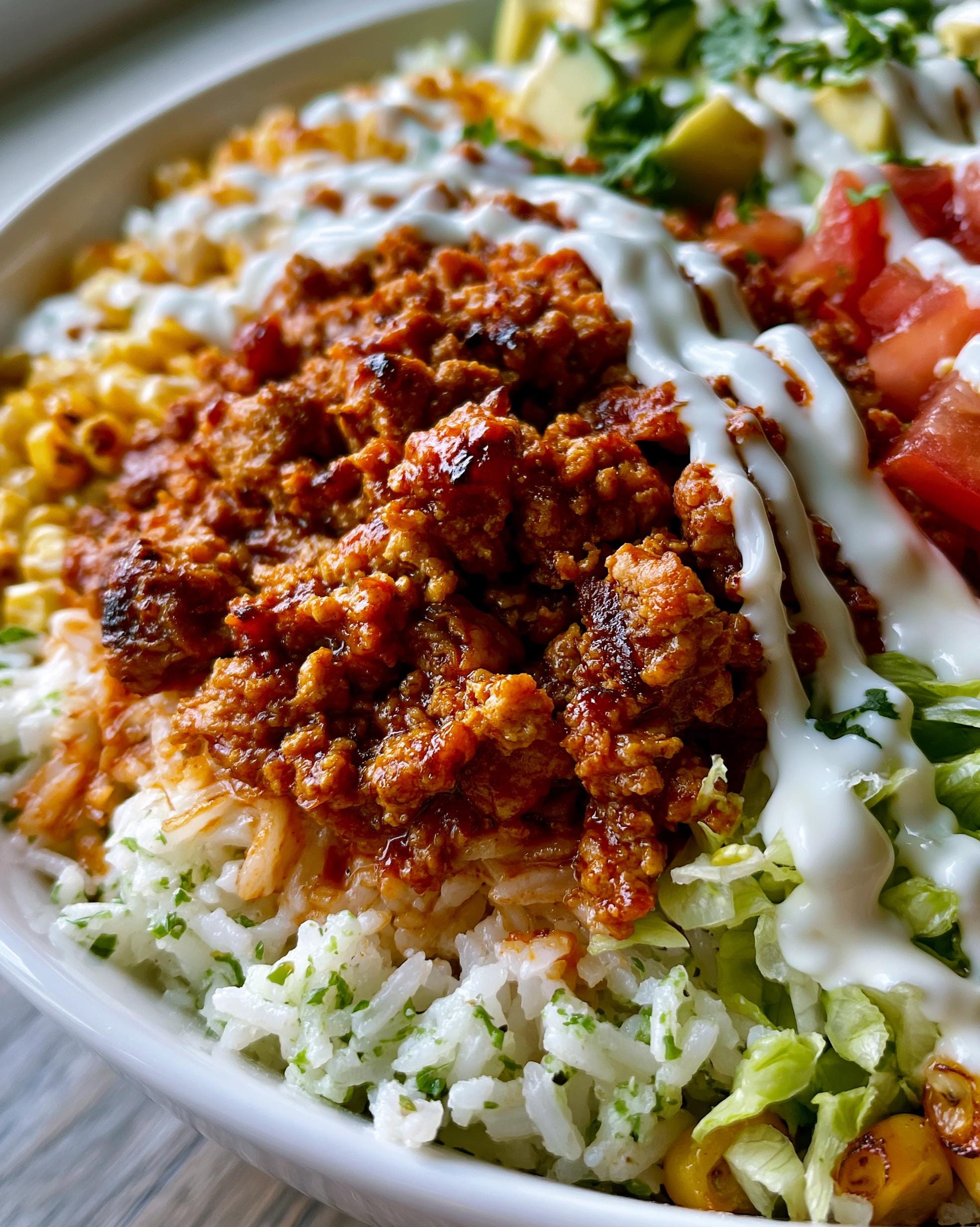 A close-up of a vibrant Turkey Taco Bowl filled with seasoned ground turkey, rice, corn, lettuce, tomatoes, avocado, and a drizzle of sour cream.